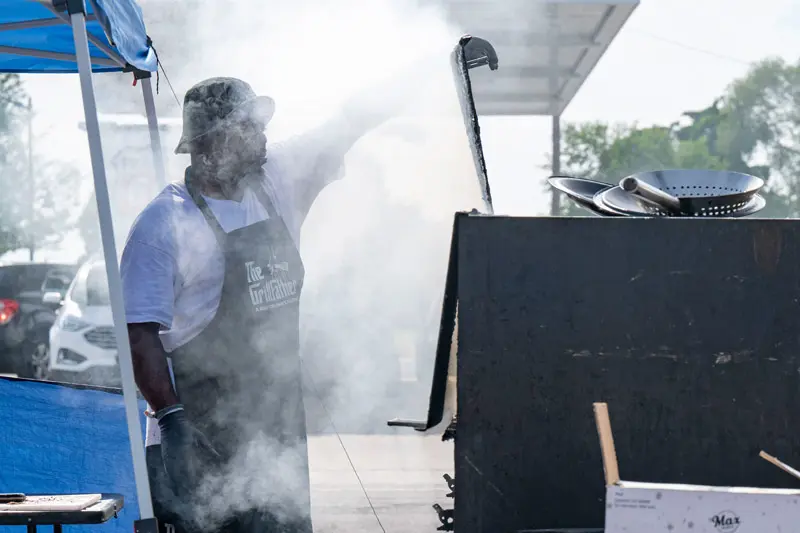 Entrepreneur Raymond Barbour stands in front of his port-a-pit grill while smoke envelopes his face.