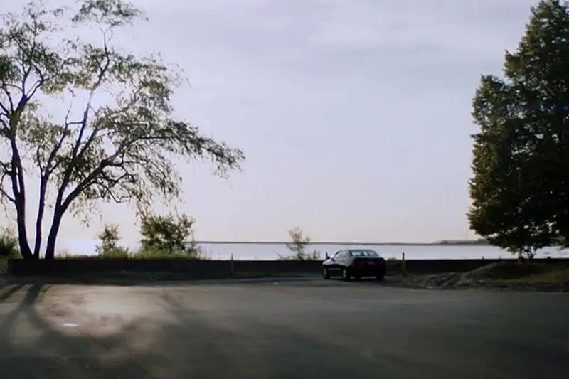 A lone car parked in a lot by the lake.