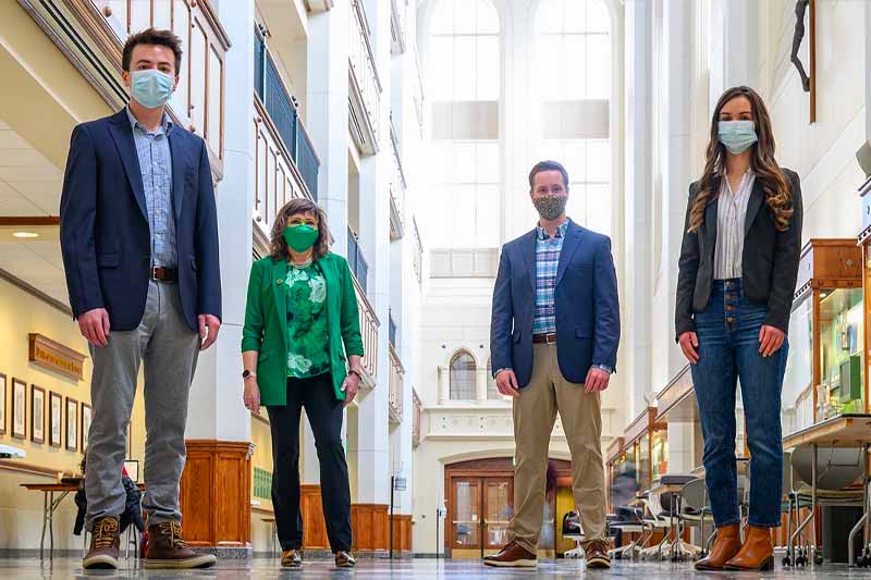 Four masked and distanced people stand in Jordan Hall of Science atrium.