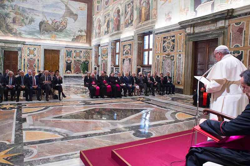 The pope stands in front of a microphone and speaks to a group of people.