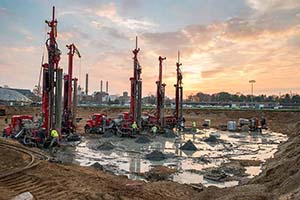 Workers installing geothermal energy system on campus at sunset.