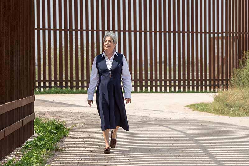 Sister Norma walks beside the border wall.