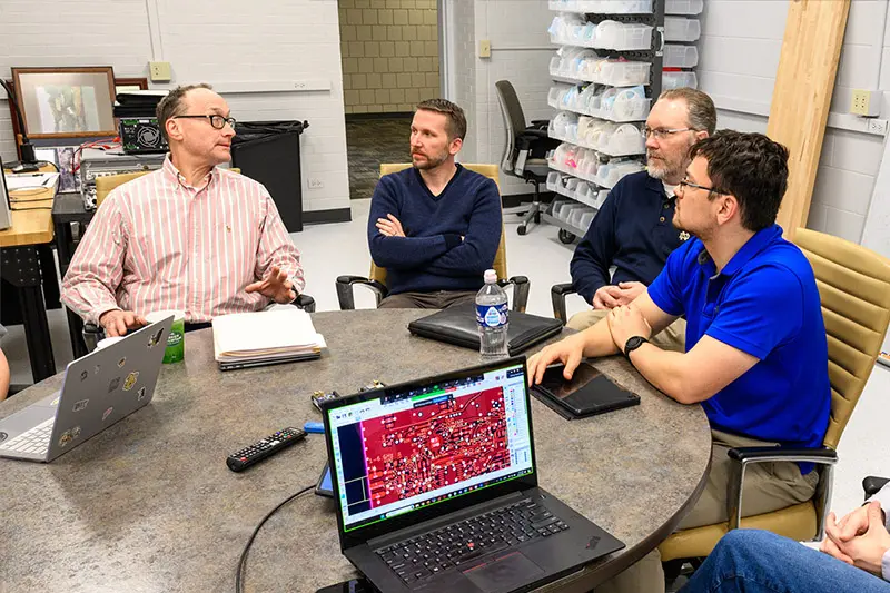 4 males, including Nick Laneman, Jonathan Chisum, and Bert Hochwald sit around a table collaborating.