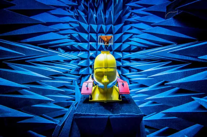 A yellow mannequin half-head sits on a desk in the electrical engineering lab with a dissected cell phone rubber banded to its ear.