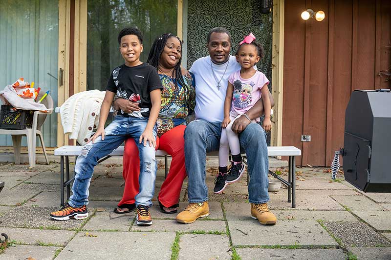 Two adults and two children pose for a photo outside of their home.