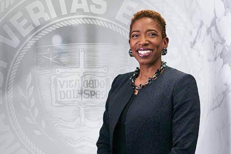 A studio shot of Carla Harris. The faded Laetare Medal is photoshopped behind her.