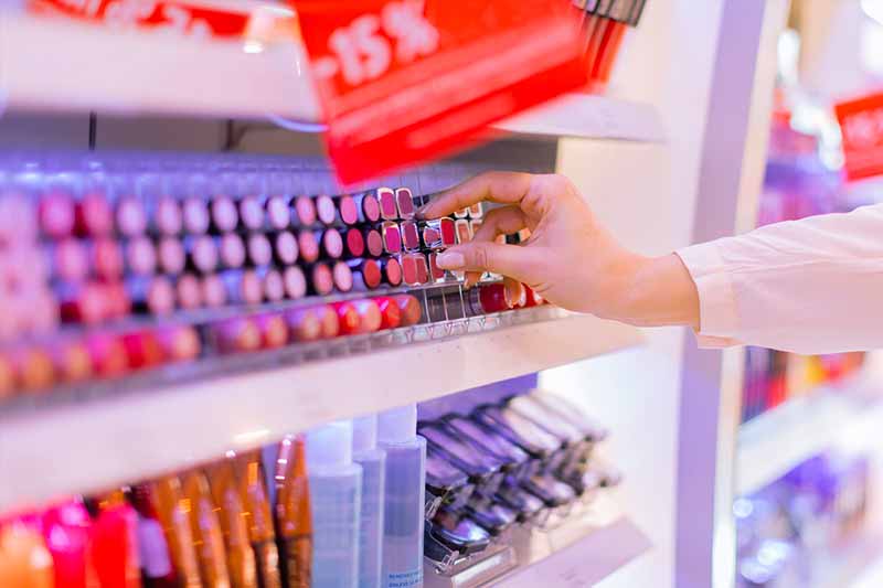 A close up of a makeup counter, a woman is taking out a lipstick from the shelf.