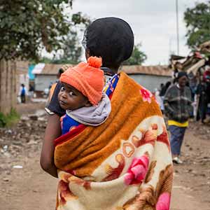 June 23, 2016; A woman carries her baby as she walks through the market in Dandora, Kenya. (Photo by Barbara Johnston/University of Notre Dame)
