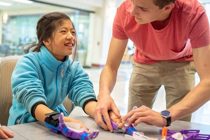 A student works with a young girl on the final fitting of a pair of 3D-printed prosthetic hands.
