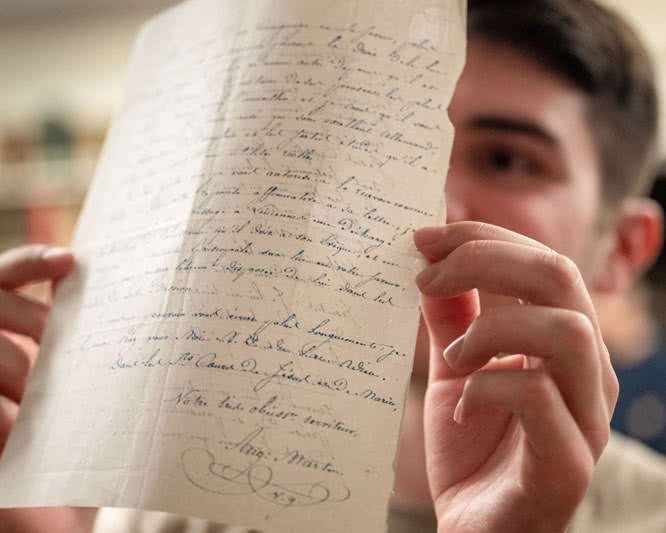 Student holding up and looking at a weathered old letter with calligraphic writing.