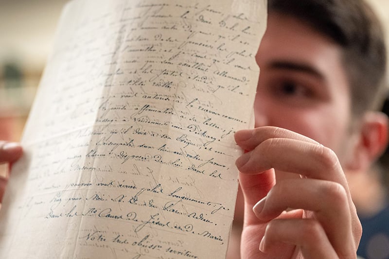 A student holds up a piece of paper with calligraphic writing on both sides of it up to the light.