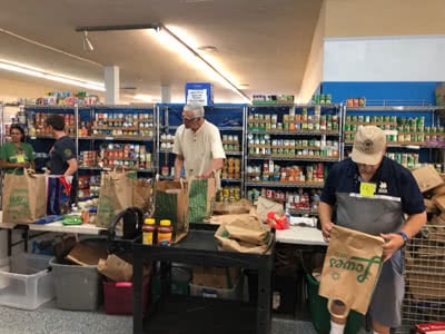 Four adults stand at a table filling paper bags with food.