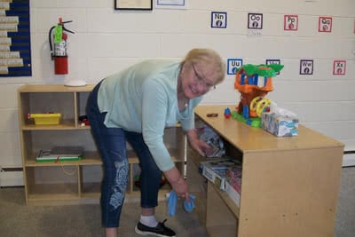 A woman cleans shelves that hold toys.