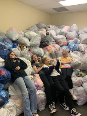 Four young ladies lay on a pile of bags filled with donated clothes.