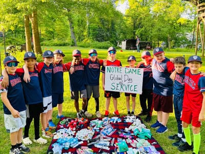 A group of boys stand in front of a blanket on the ground that displays all the hygiene products they collected.