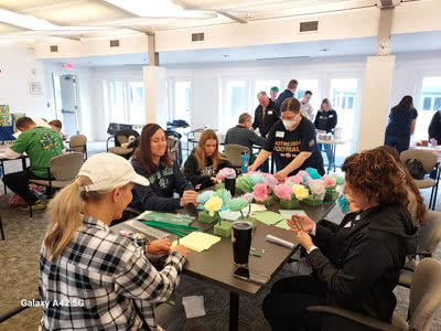 A group of women sit at a table creating tissue paper flowers.