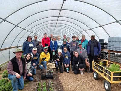 A large group of volunteers pose for a photo inside a greenhouse.