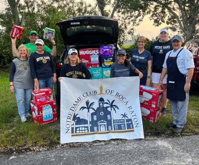 A group of people stand by a car with the tailgate open showing all the boxes of diapers they collected.