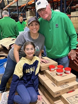 Three people pose for a photo near boxes of food.