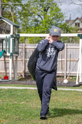 A boy carries a trash bag across a backyard.