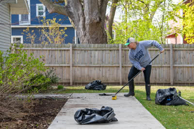 A woman cleans a sidewalk with a broom.