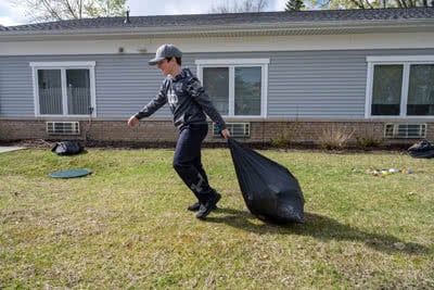 A boy drags a bag of trash across a backyard.