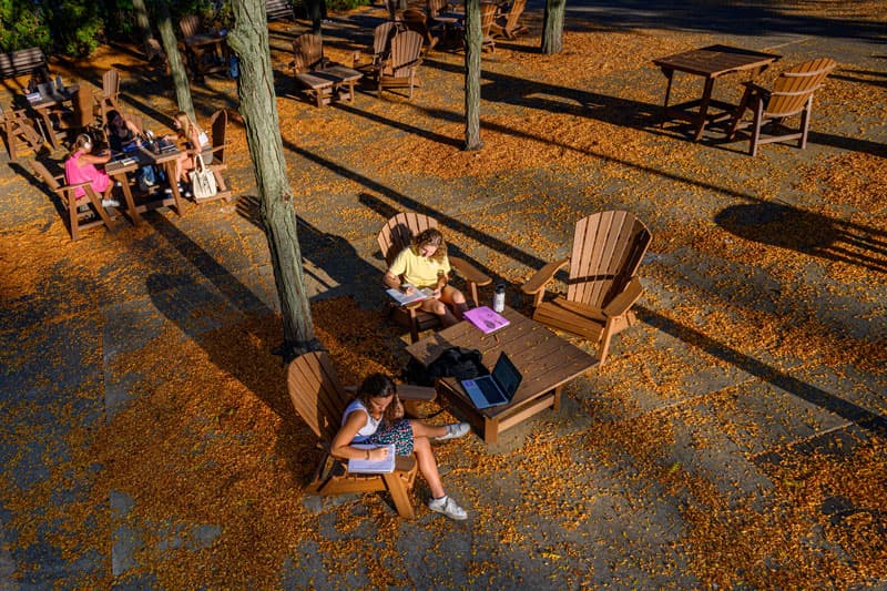 A small group of students study at the tables outside LaFortune surrounded by Fall leaves.