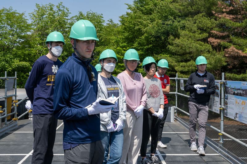 A group of students wearing green hard hats stand outside the nuclear plant in Fukushima.