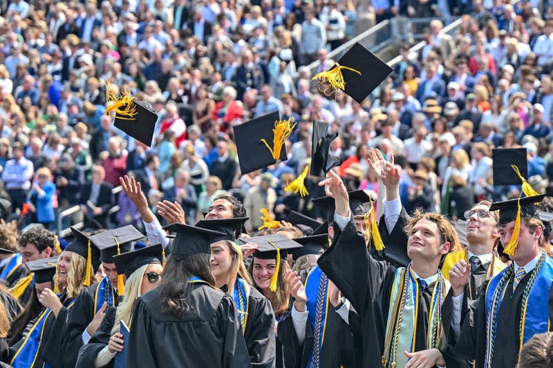 A crowd of graduates throw caps in the air to celebrate graduation.