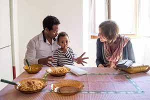 A man is having an expressive converstaion with another as his son sits on his lap at a dinner table.