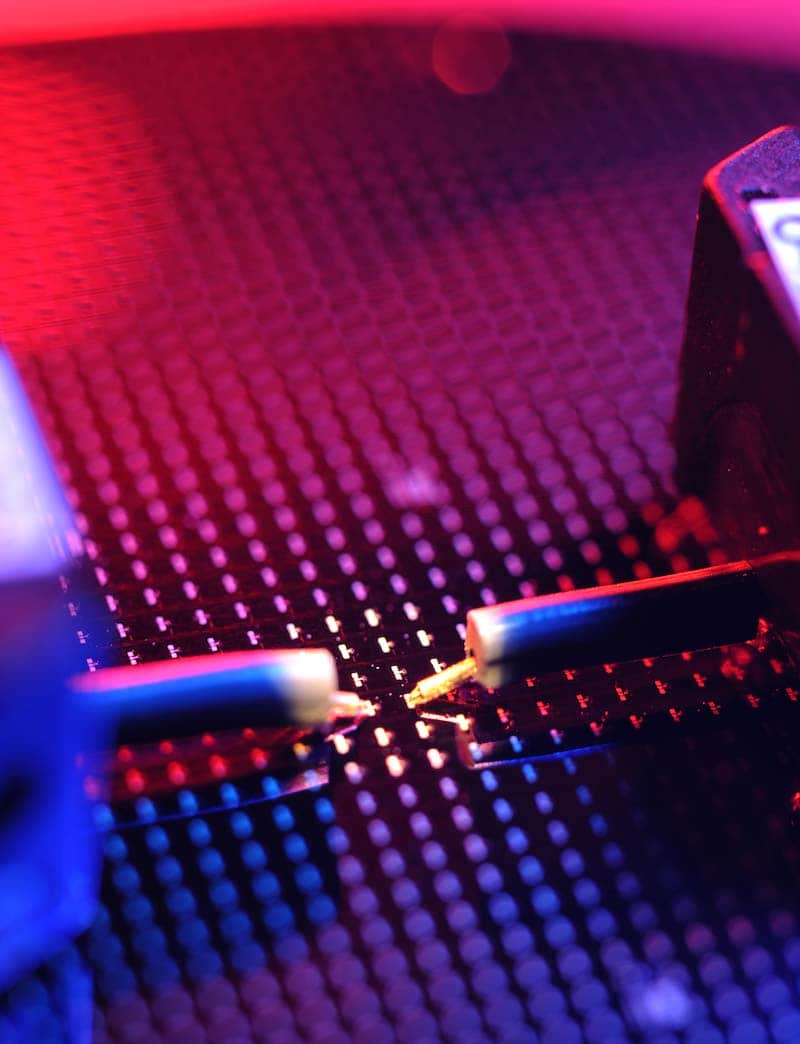 A close up of a silicon wafer with pink and red lighting.