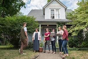 A group of people stand in front of a home with lead testing kits.