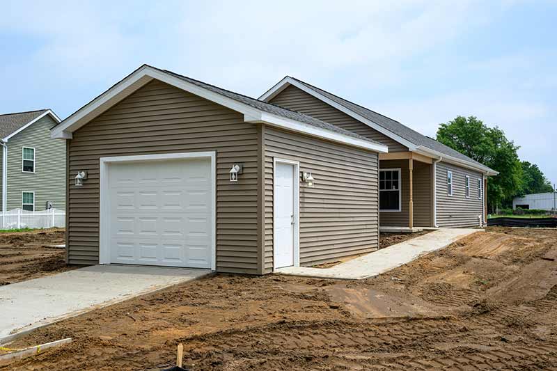 A detached garage with a concrete driveway that leads up to the garage door. A side door and concrete path leads to the back of the home.