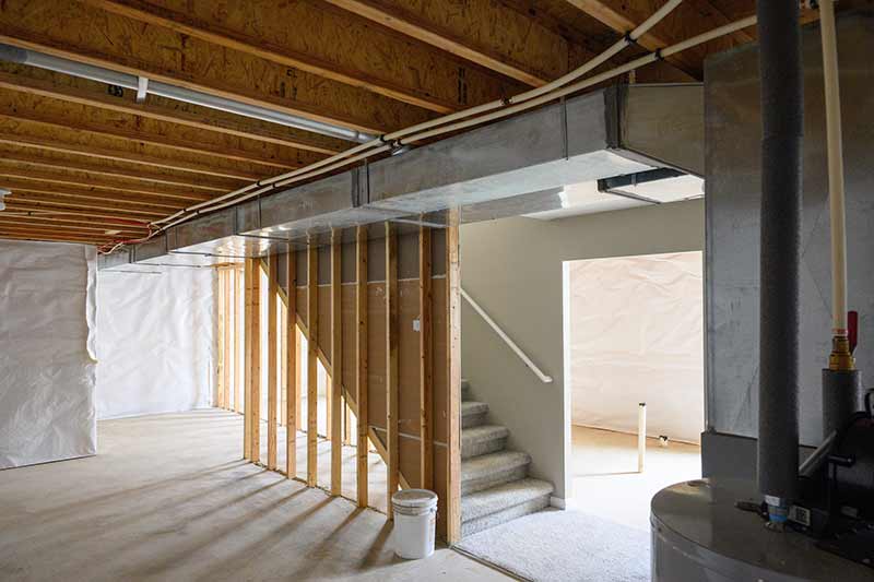 A partially finished basement with a staircase in the middle of the room. Part of the water heater can be seen in the right corner.