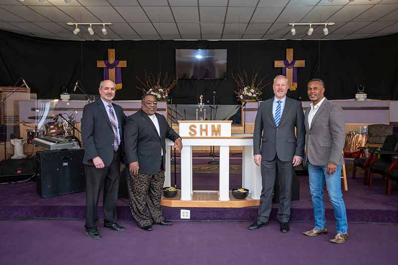 Four men stand near a podium inside Sweet Home Ministries.