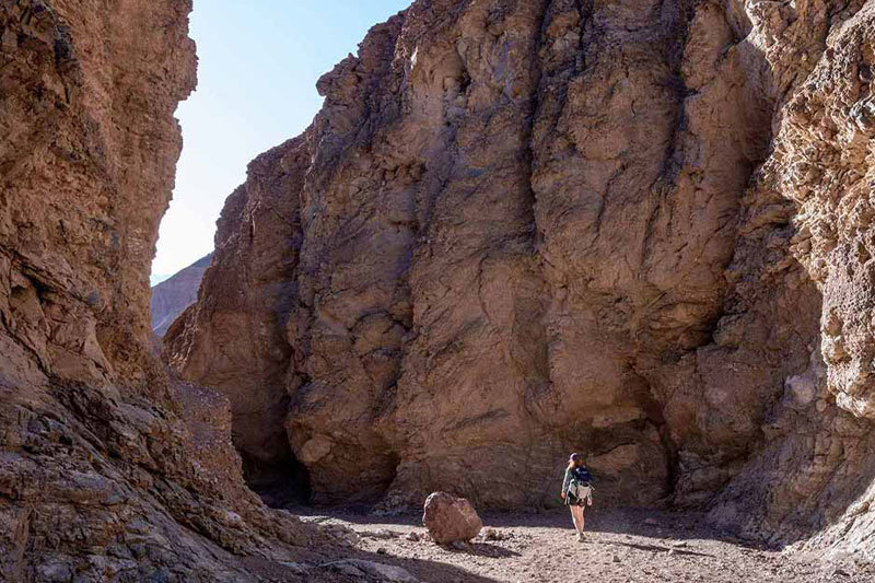 An individual walks between two large rocky mountains