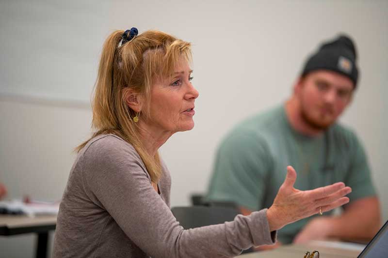 A woman speaks in class, with her hand gesturing openly.