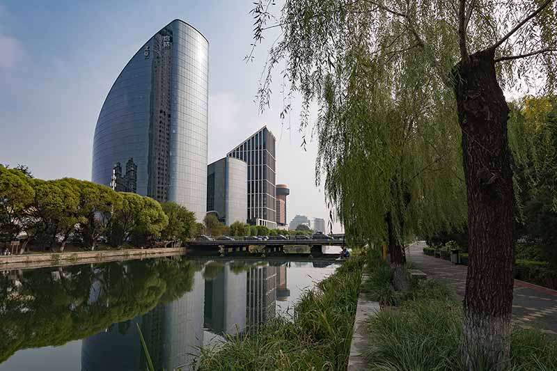 A park full of trees and a river in the foreground of the Genesis Beijing building which houses the Notre Dame Beijing Global Gateway.