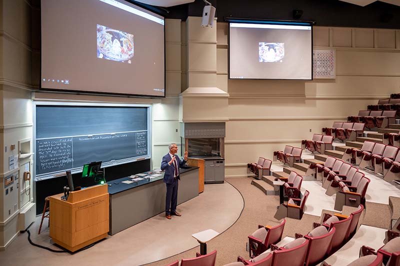 A man teaches to a large empty auditorium classroom.
