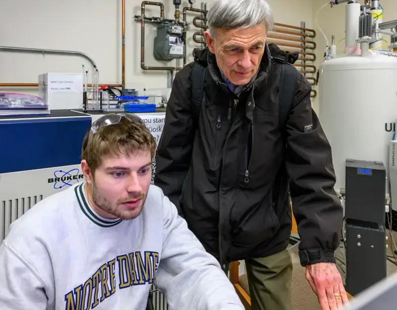 Professor Paul Helquist stands next to undergraduate researcher Nick Dolphin at an uclear Magnetic Resonance machine.
