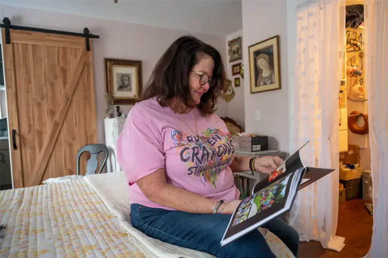 Mom Gail Koujaian sits on a bed looking through a photo album.