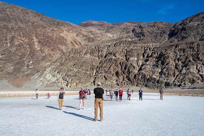 A man stands with his back to the camera, looking at a group of students examine the Badwater Basin.
