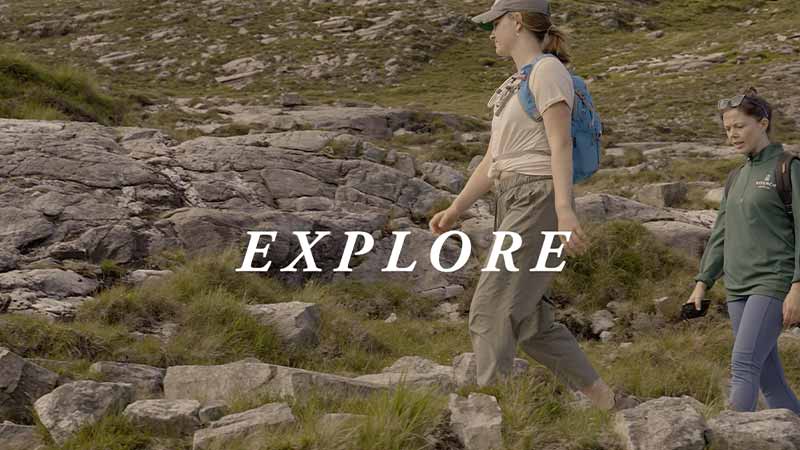 A woman hiking through a rocky field, 'Explore' text on top of the image.
