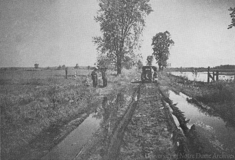 An archival photo of a car and three men stopped on a muddy road.