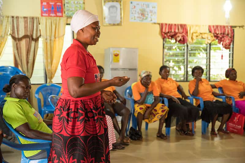 A woman holds out her hand as she stands speaking to a group of other woman inside of a building.