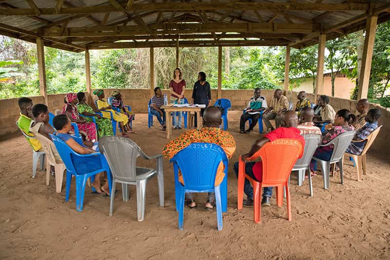 Two women speak while standing up as others are sitting in chairs forming a circle.