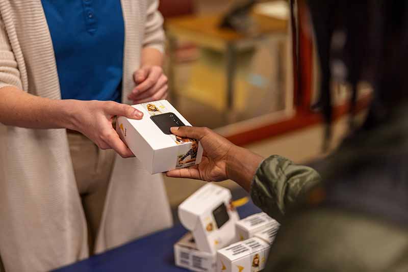 A woman hands a wifi hotspot box to a student.