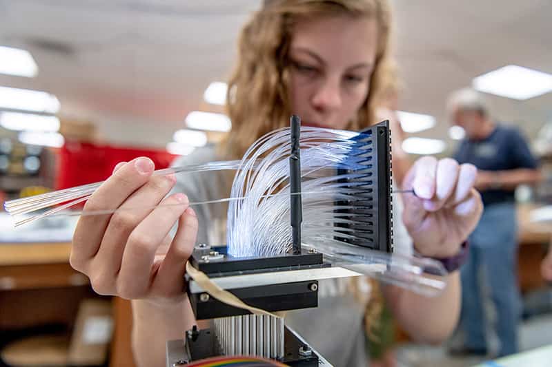 A female student threads fiber optics through anodized metal plates the size of postcards.