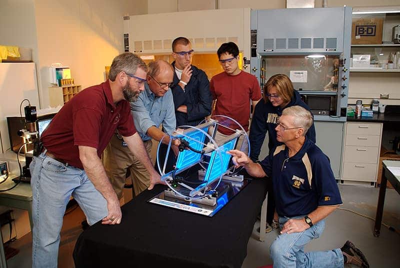 Teachers and professors gather together observing a device.