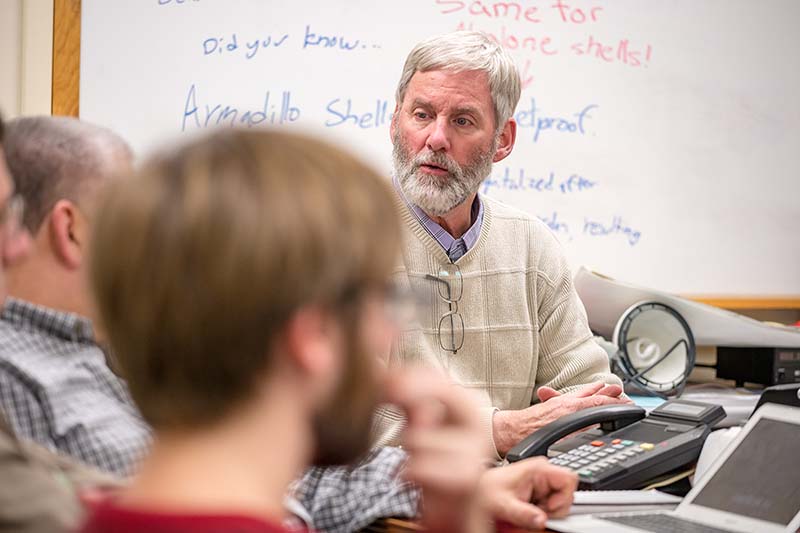 A male teacher sits at the head of the table.